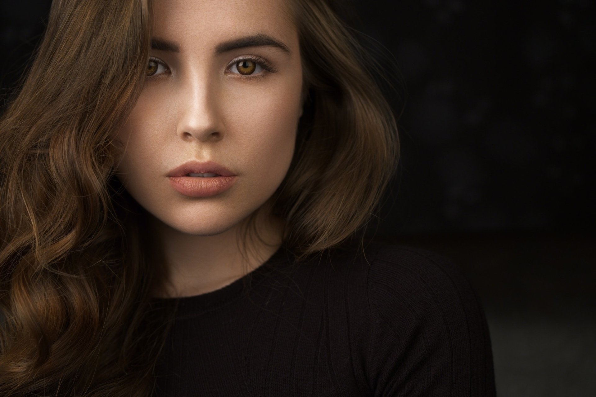 HD desktop wallpaper of a brunette model with brown eyes, captured in a close-up portrait against a dark background.