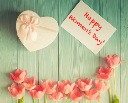 HD desktop wallpaper of a heart-shaped gift box and pink flowers on a wooden surface, with a card reading Happy Women's Day! A delightful image celebrating the holiday.