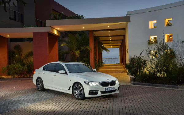 White BMW 5 Series car parked outside a modern house at dusk, captured in 4K Ultra HD quality for a PC desktop wallpaper.
