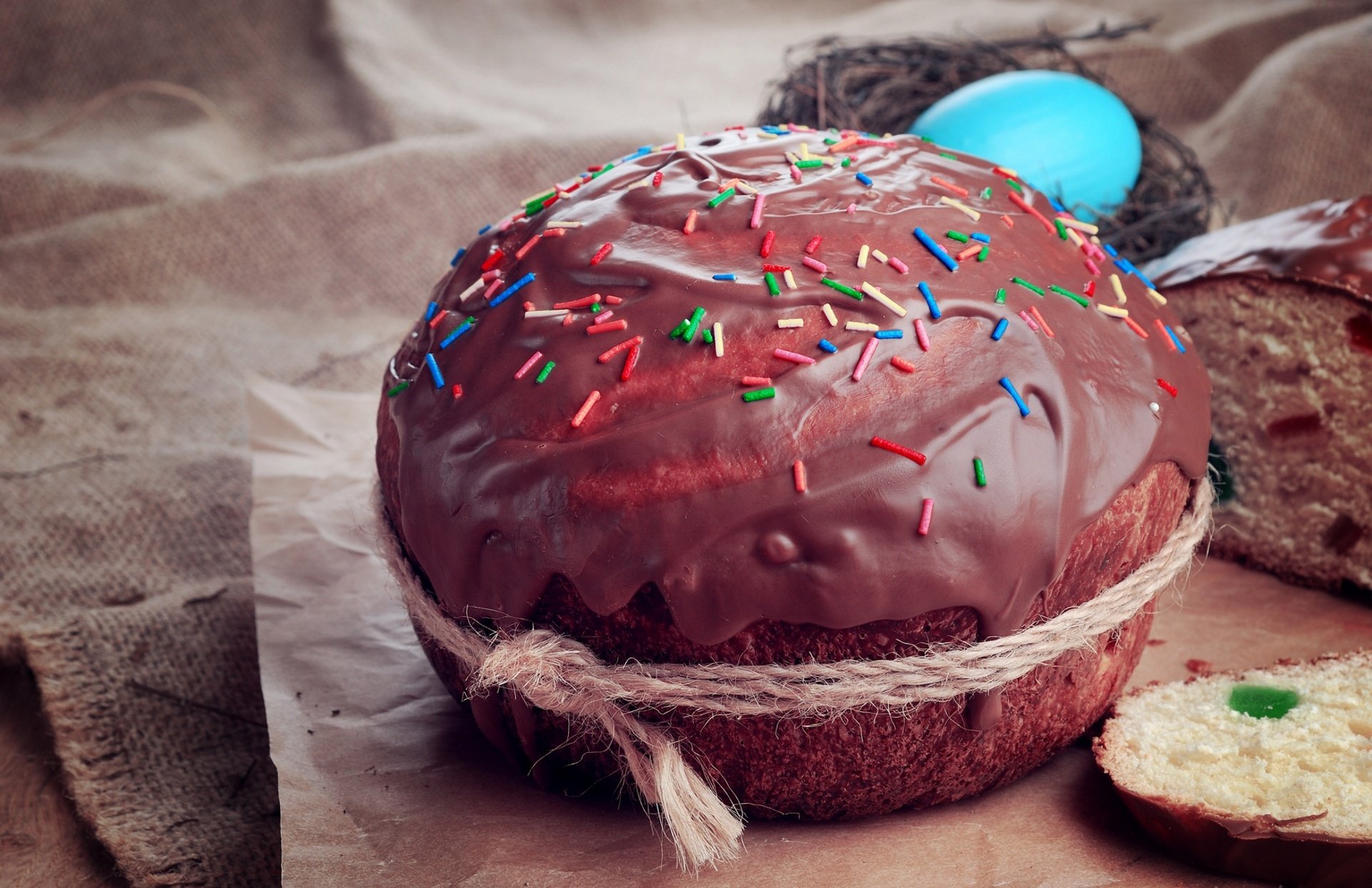 HD desktop wallpaper featuring a chocolate-covered pastry with colorful sprinkles, set on rustic fabric, highlighting rich textures of cake and festive decoration.