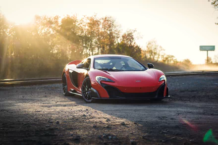 A stunning HD desktop wallpaper features a sleek, red McLaren 675LT supercar parked on a gravel road with a backdrop of trees and a setting sun.