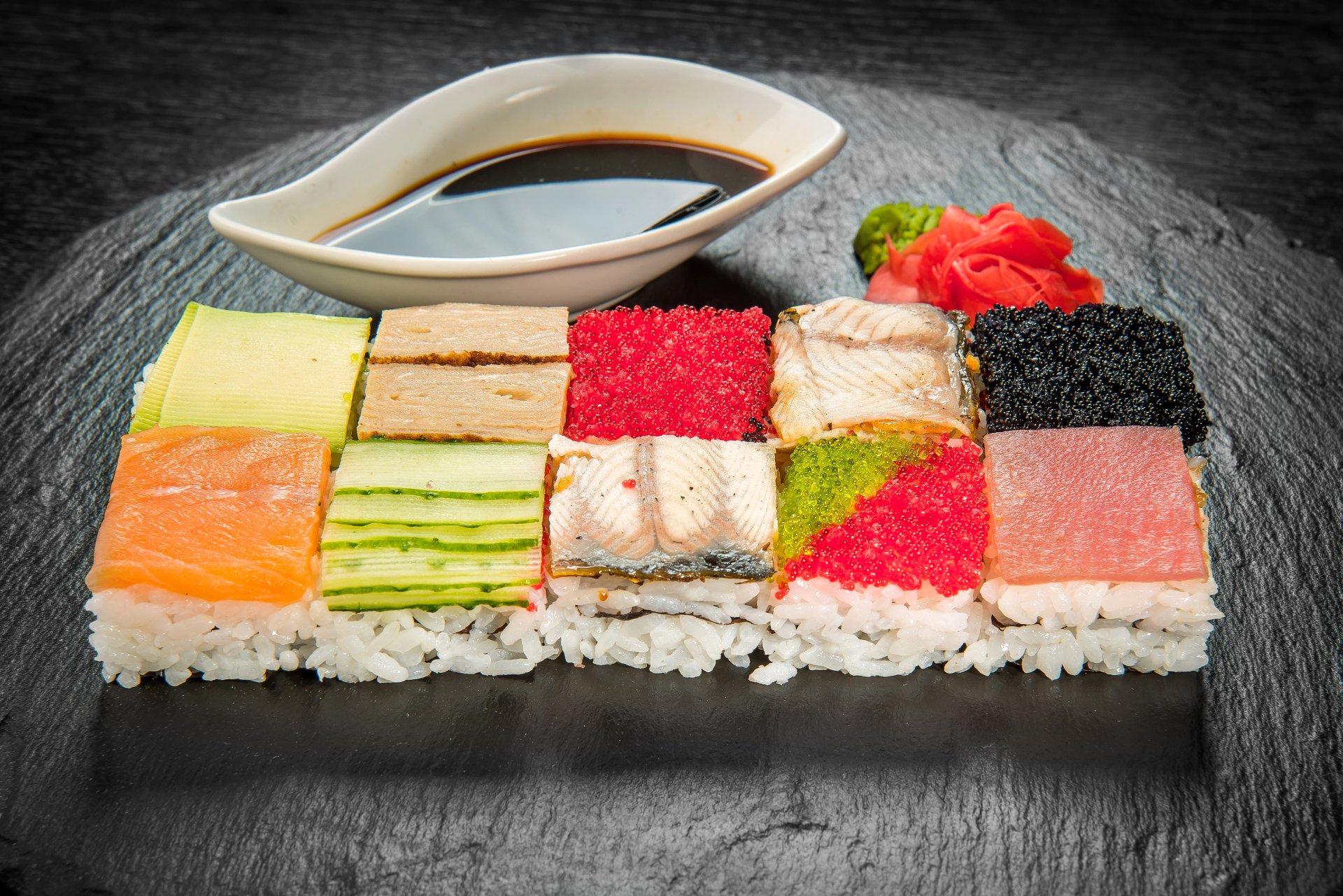 5K Ultra HD PC desktop wallpaper of assorted sushi mosaic on rice — colorful fish, roe, cucumber and tamago squares on a slate board with soy sauce, pickled ginger and wasabi.