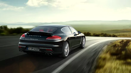 Black Porsche Panamera Turbo on a winding country road at sunset, rear three-quarter view, 2K Quad HD PC desktop wallpaper/background.