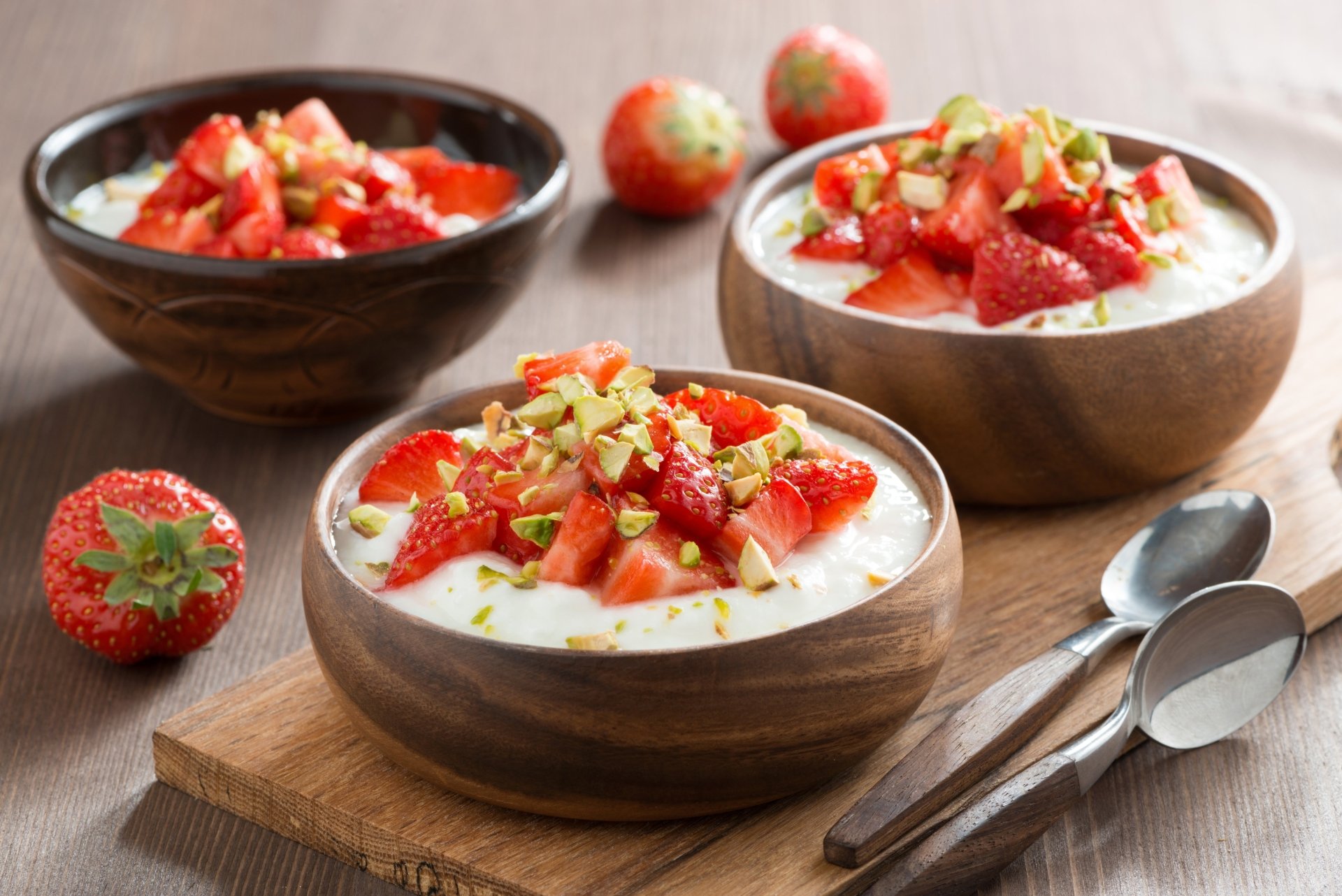 A 4K Ultra HD desktop wallpaper showing wooden bowls filled with creamy yogurt topped with fresh strawberries and chopped nuts, accompanied by spoons and whole strawberries.