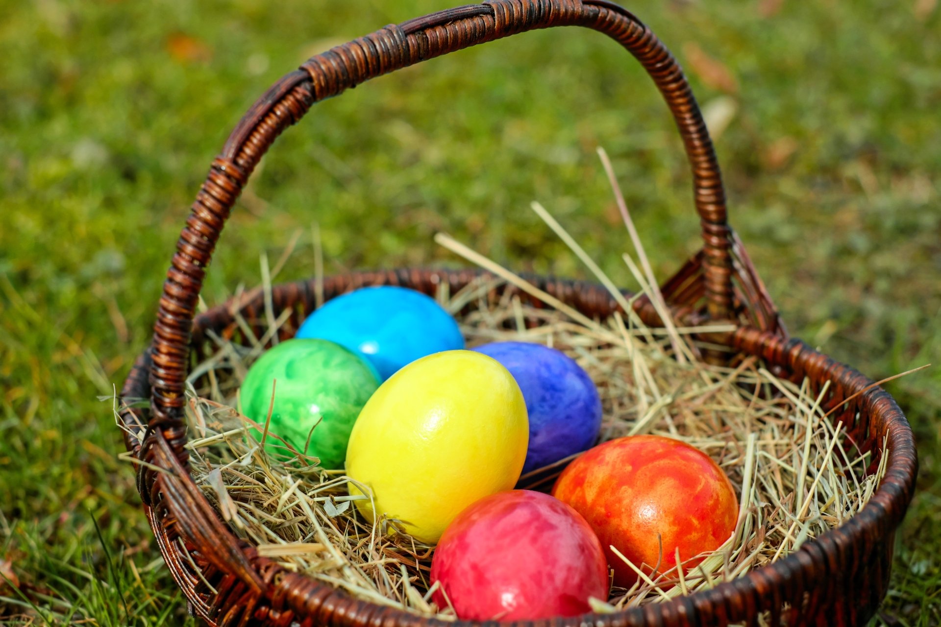 A rustic wicker basket filled with colorful Easter eggs resting on hay, set against a grassy background, captured in vibrant 4K Ultra HD for PC desktop wallpaper.