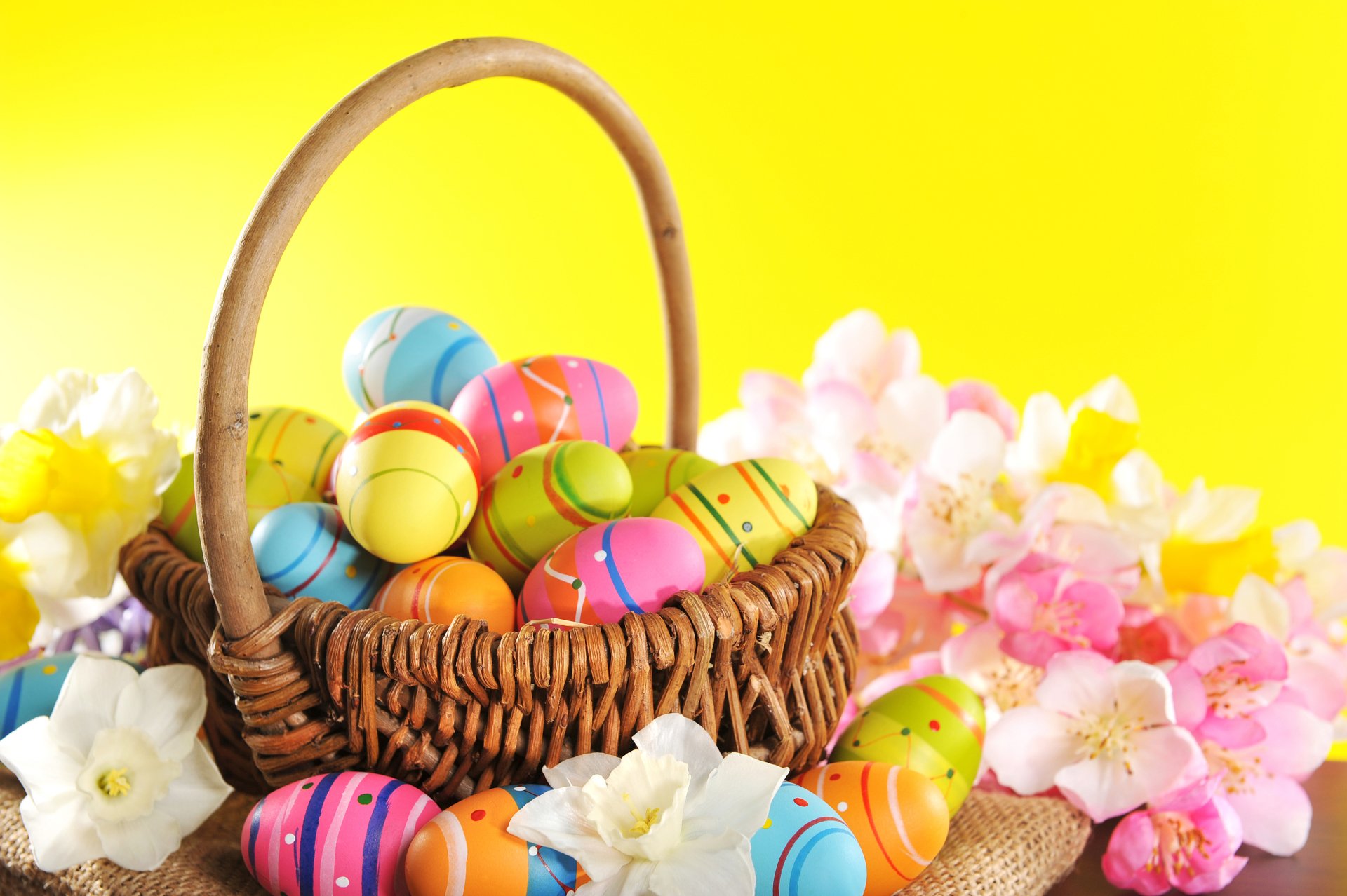 A colorful wicker basket filled with vibrant Easter eggs surrounded by pastel flowers against a bright yellow background, shown in 4K Ultra HD as a desktop wallpaper.