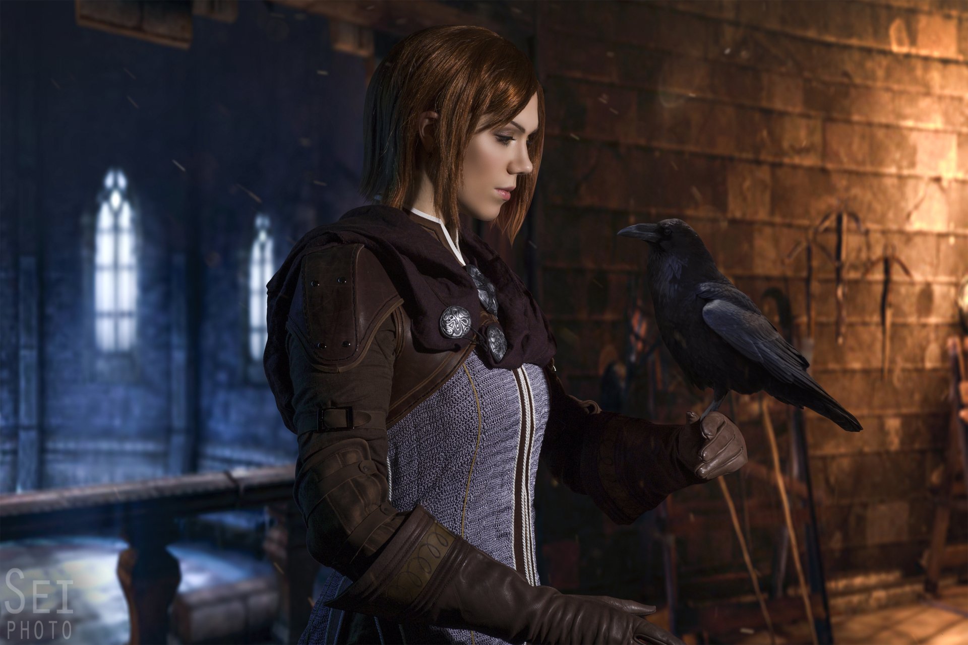 HD PC desktop wallpaper featuring a woman cosplaying Leliana from Dragon Age: Inquisition, set against a dimly lit medieval interior with stone walls and stained glass windows.