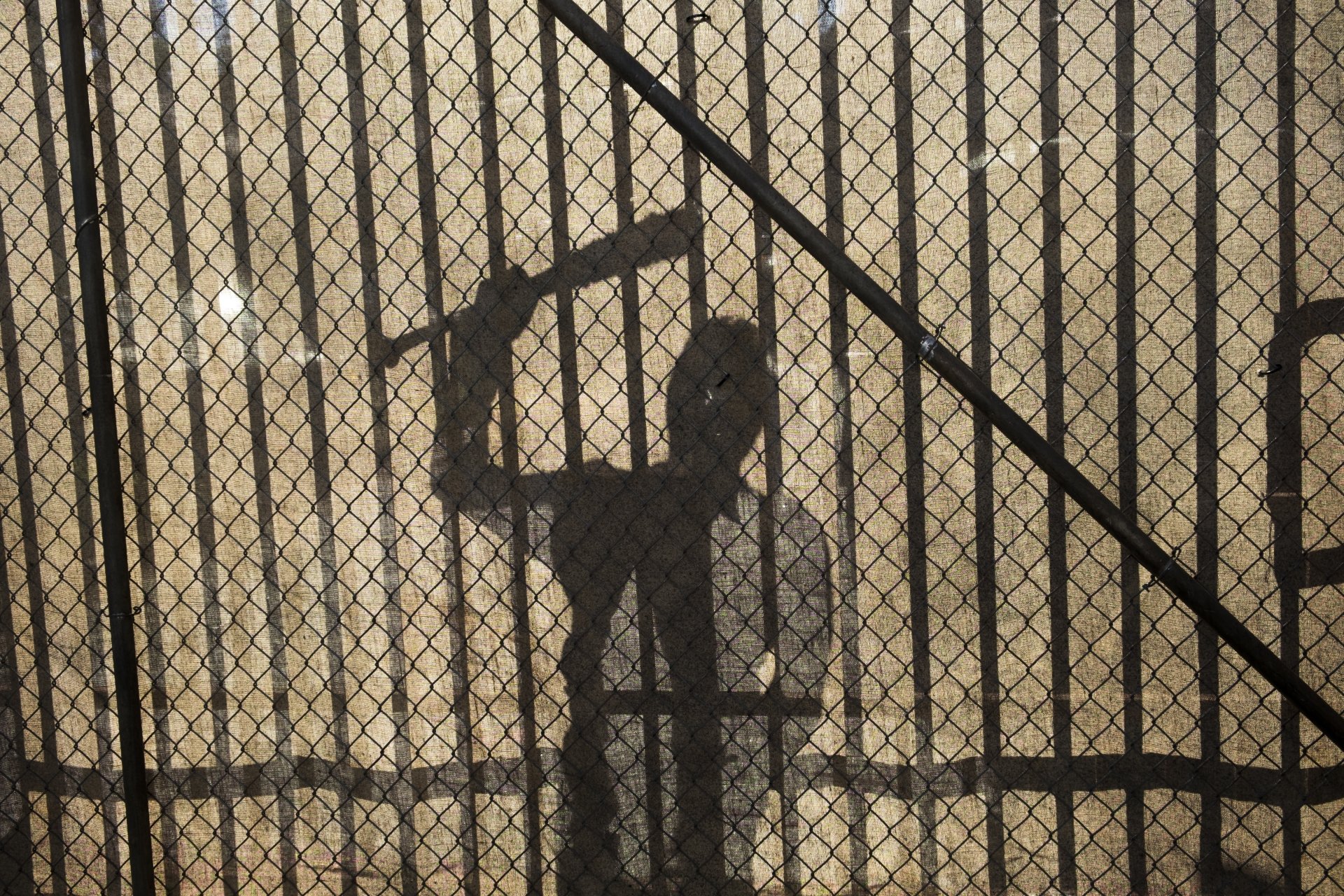 Shadowed silhouette of Negan, played by Jeffrey Dean Morgan in The Walking Dead, wielding a bat behind a chain-link fence in this 4K Ultra HD PC desktop wallpaper.