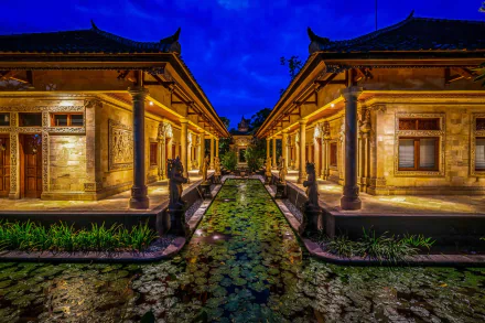 An HD desktop wallpaper featuring a tranquil lily pad-filled waterway between two beautifully lit architectural structures in a hotel in Bali, Indonesia.