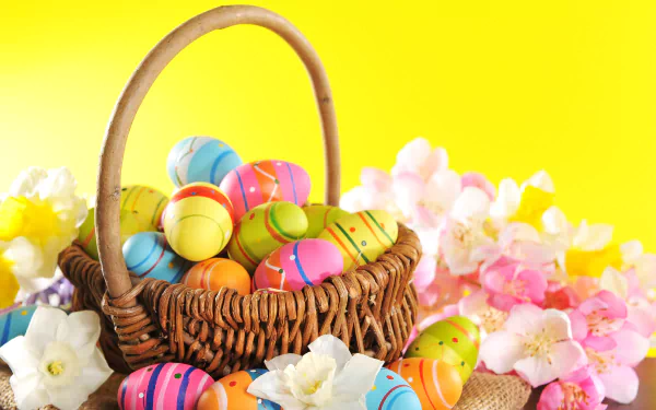 A colorful wicker basket filled with vibrant Easter eggs surrounded by pastel flowers against a bright yellow background, shown in 4K Ultra HD as a desktop wallpaper.