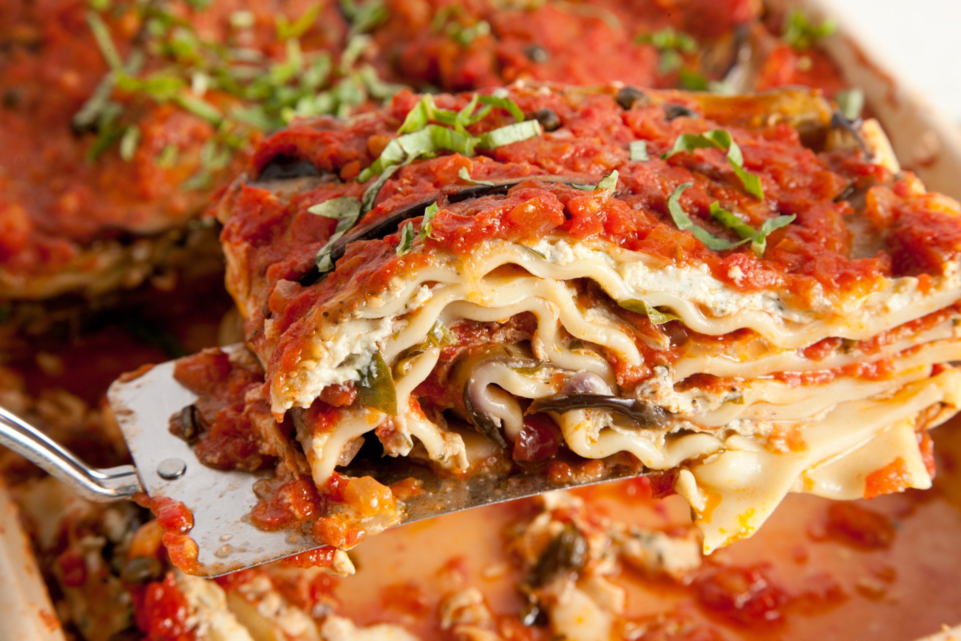 Close-up HD desktop wallpaper of a delicious, layered lasagna meal topped with tomato sauce and fresh herbs.