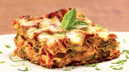 HD PC desktop wallpaper and background showing a hearty lasagna meal: close-up of a cheesy, layered slice of food garnished with basil on a white plate.