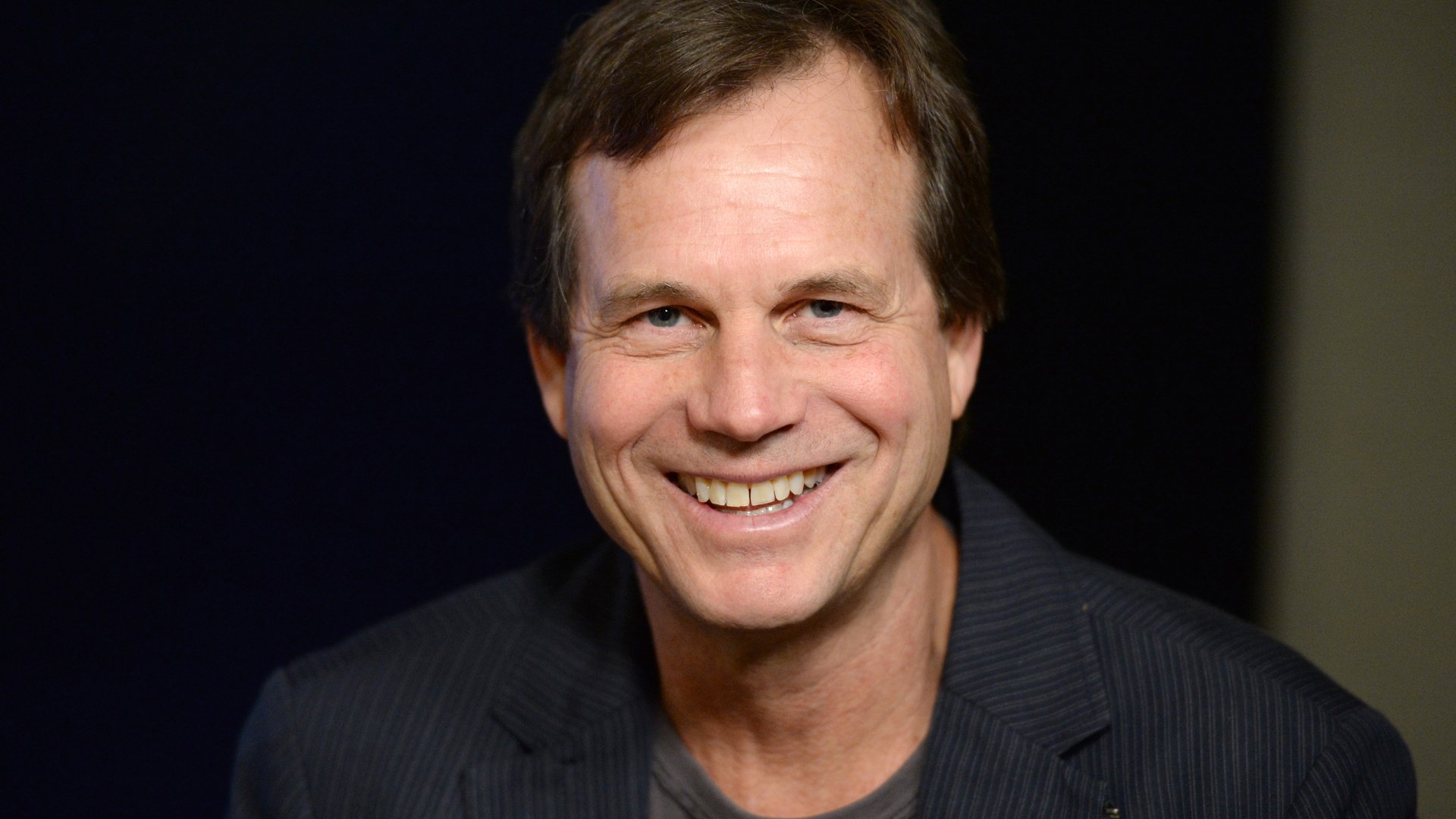 A captivating HD desktop wallpaper featuring celebrity Bill Paxton, showcasing his warm smile and charismatic presence against a dark background.