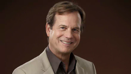 HD desktop wallpaper featuring a smiling man in a beige jacket against a brown background.