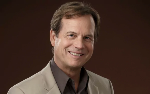 HD desktop wallpaper featuring a smiling man in a beige jacket against a brown background.