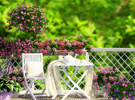 A serene porch scene featuring a white chair and table adorned with a teapot and fabric, surrounded by blooming pink spring flowers and lush green plants, captured in HD photography.
