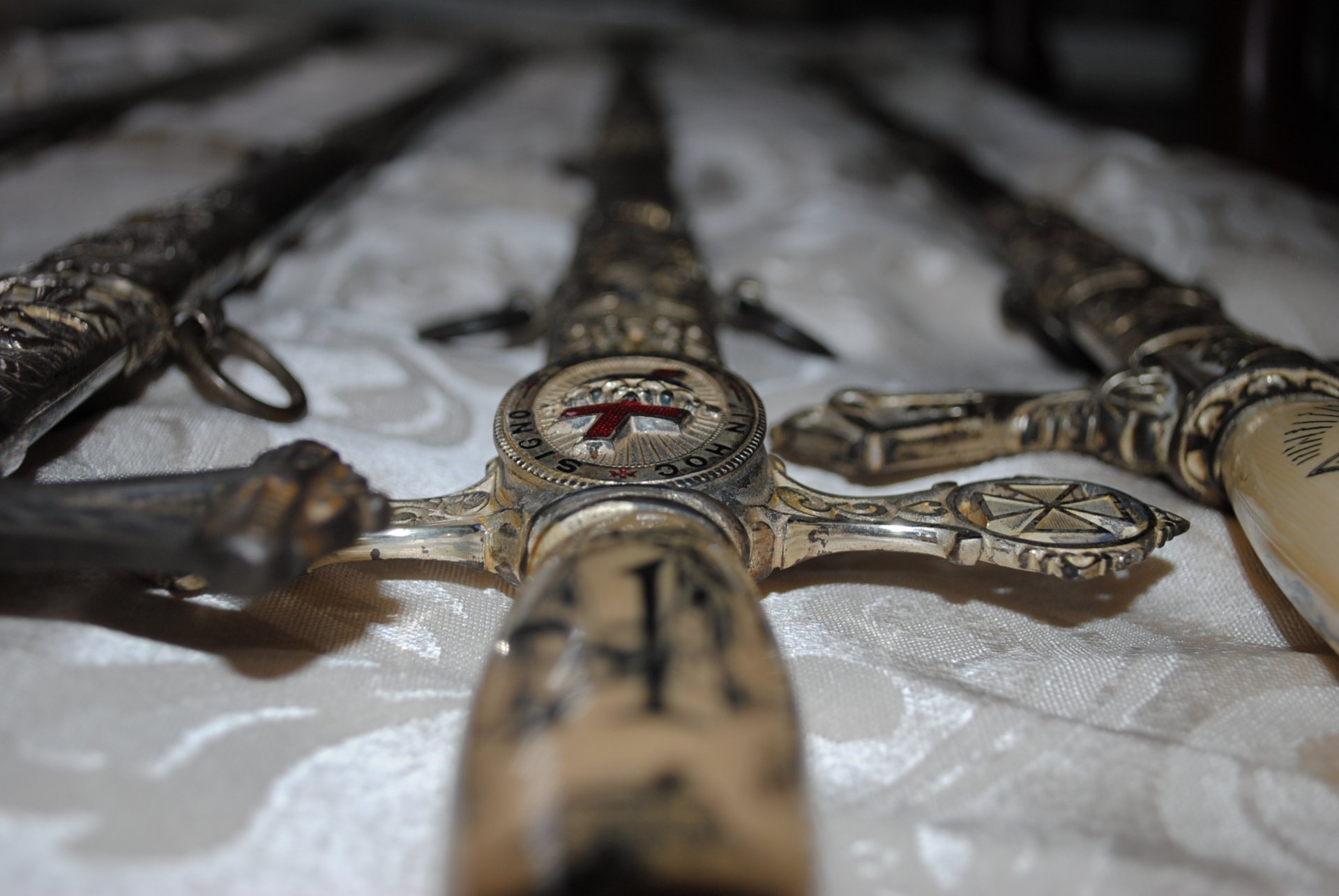 Detailed close-up of ornate man-made swords arranged on a textured surface, showcasing intricate designs and craftsmanship. An engaging HD wallpaper for sword enthusiasts.