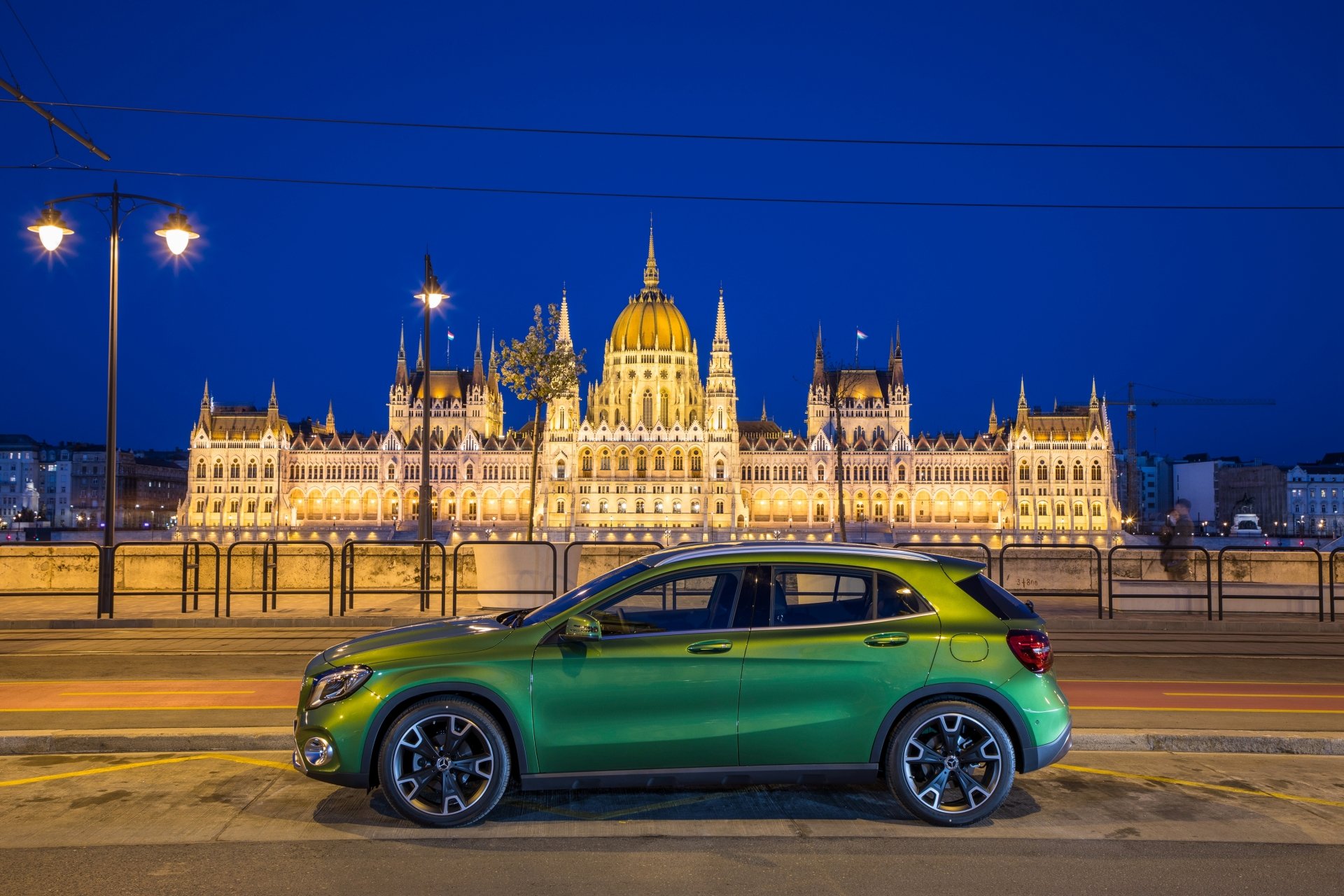 Green Mercedes‑Benz GLA‑Class SUV parked at night in front of the illuminated Hungarian Parliament building — 4K Ultra HD PC desktop wallpaper background.