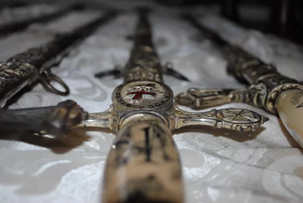 Detailed close-up of ornate man-made swords arranged on a textured surface, showcasing intricate designs and craftsmanship. An engaging HD wallpaper for sword enthusiasts.