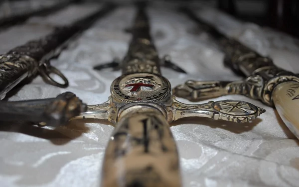 Detailed close-up of ornate man-made swords arranged on a textured surface, showcasing intricate designs and craftsmanship. An engaging HD wallpaper for sword enthusiasts.