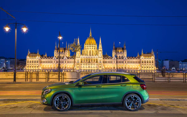 Green Mercedes‑Benz GLA‑Class SUV parked at night in front of the illuminated Hungarian Parliament building — 4K Ultra HD PC desktop wallpaper background.