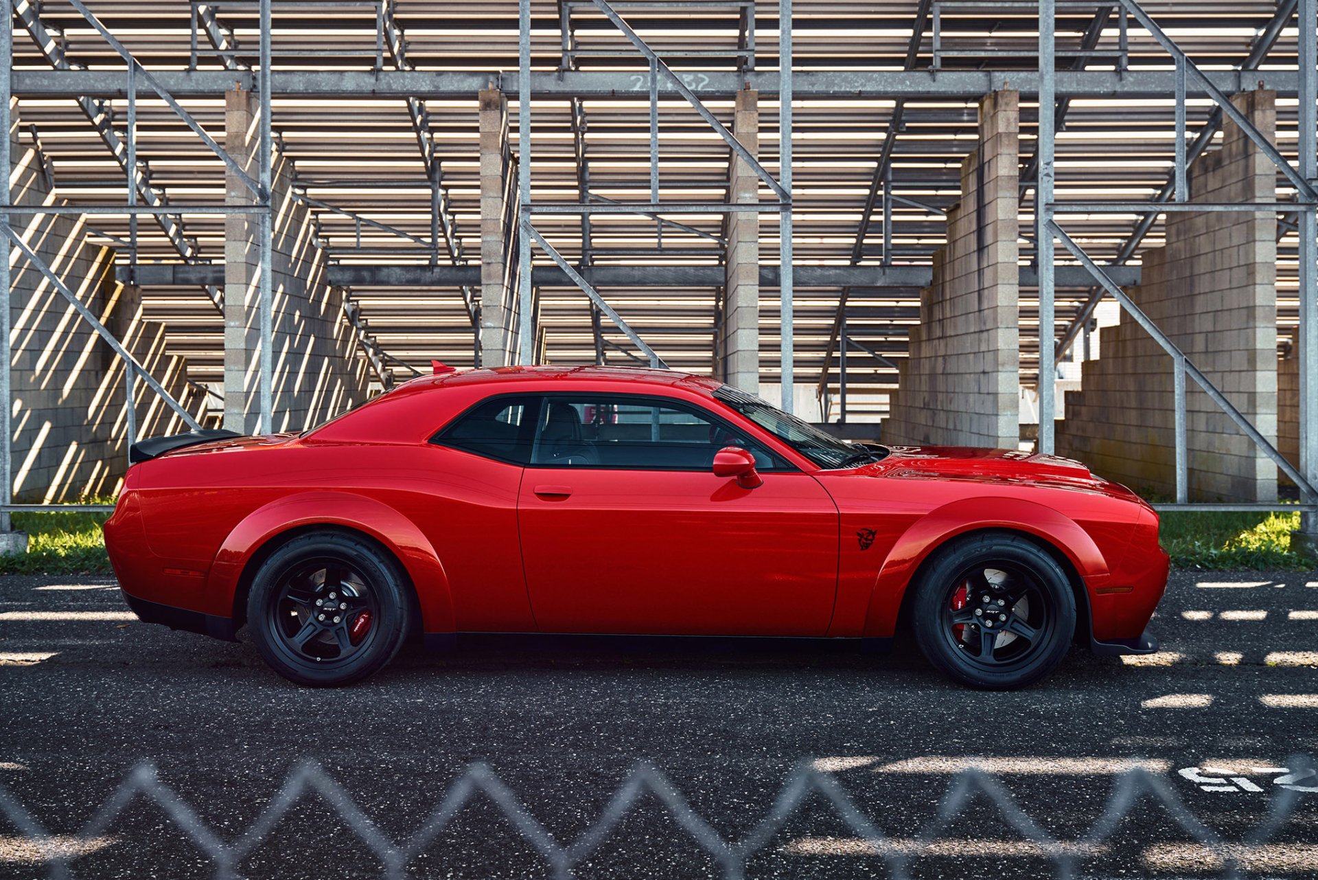 Side view of a red Dodge Challenger SRT Demon muscle car parked in front of an industrial metal structure, captured in HD for a PC desktop wallpaper and background.