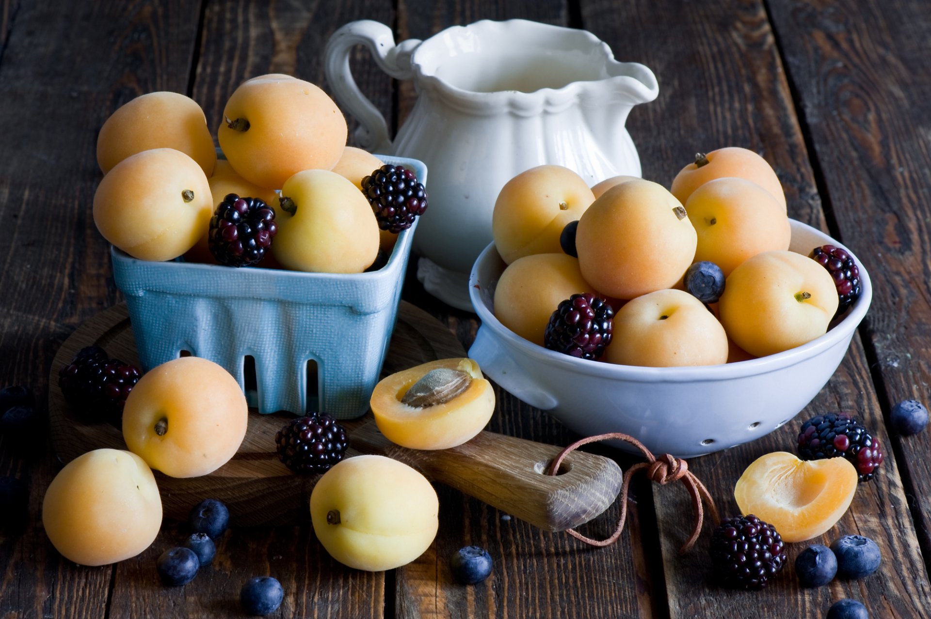 HD PC desktop wallpaper still life of apricots, blackberries and blueberries in bowls and a blue berry basket on a rustic wooden table, one apricot halved.