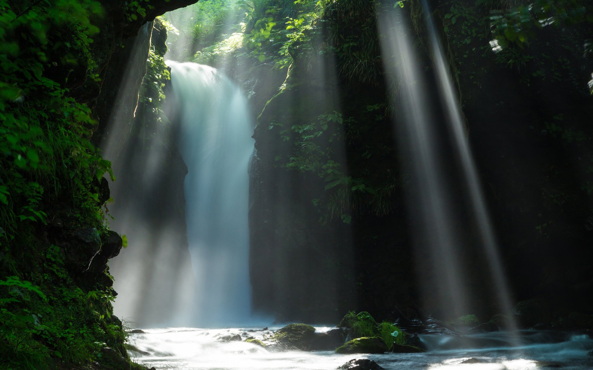 2K Quad HD PC desktop wallpaper/background: sunbeams and soft light piercing a lush forest over a cascading waterfall, mist rising into a tranquil nature scene.