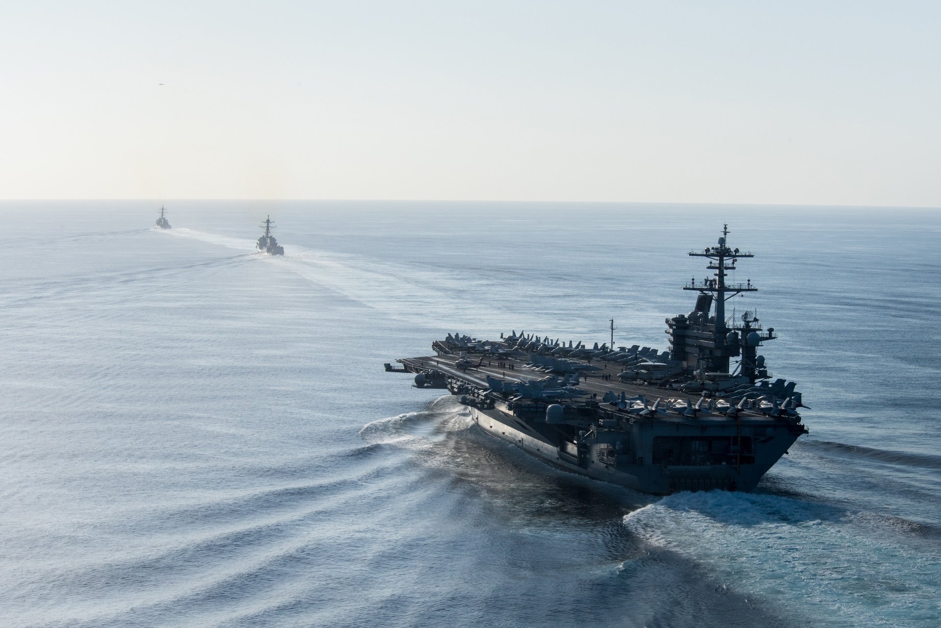HD PC desktop wallpaper: aircraft carrier USS Theodore Roosevelt (CVN-71) steaming at sea with escort warships, flight deck visible and wake trailing behind.