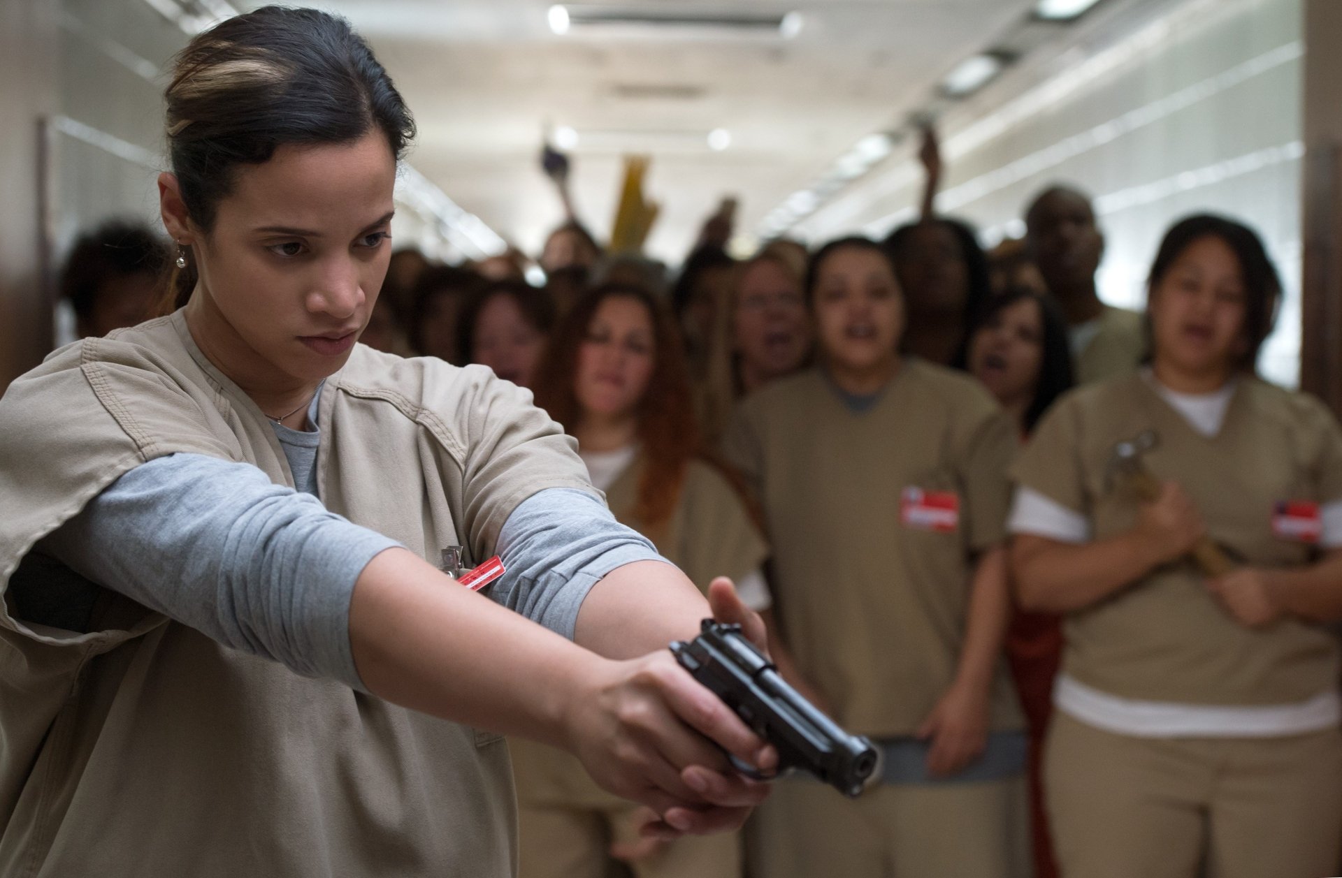 2K Quad HD desktop wallpaper of a TV prison-drama scene: a female inmate aims a handgun while other inmates shout behind her.