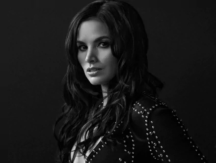 Monochrome HD PC desktop wallpaper of a celebrity actress in black-and-white, long dark hair and studded jacket, gazing confidently against a dark studio background.