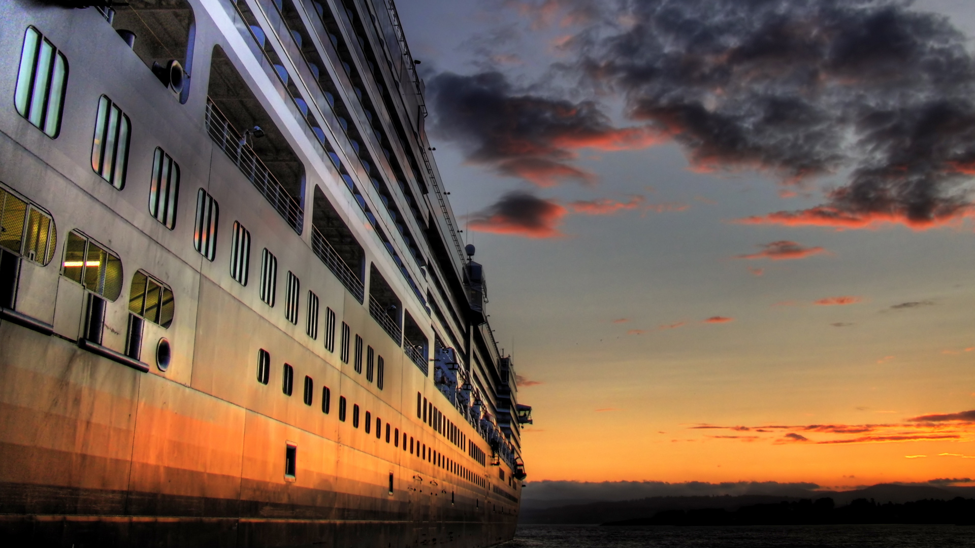 Cruise ship sailing towards a colorful sunset over a cloudy sky.