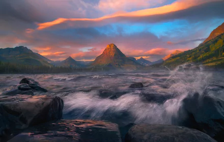 HD desktop wallpaper depicting a serene lake at sunset in Glacier National Park, with vibrant clouds and a mountainous backdrop.