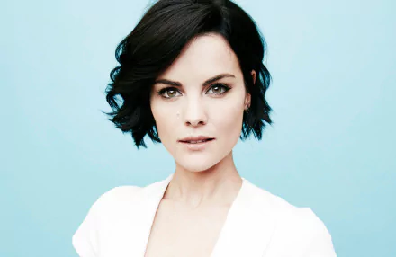 HD PC desktop wallpaper: close-up portrait of a woman with short dark hair, direct gaze and light makeup against a pale blue background.