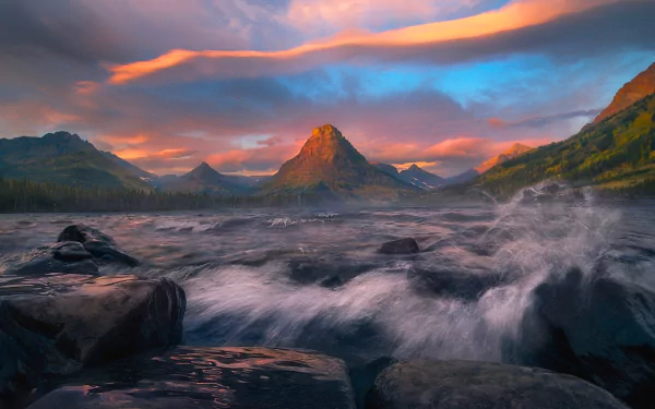 HD desktop wallpaper depicting a serene lake at sunset in Glacier National Park, with vibrant clouds and a mountainous backdrop.