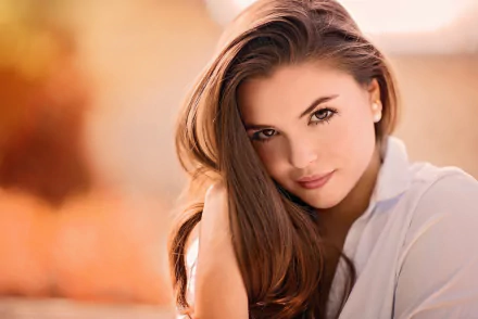 HD desktop PC wallpaper of a brunette woman model with brown eyes, close-up of her face against a soft, warm blurred background.