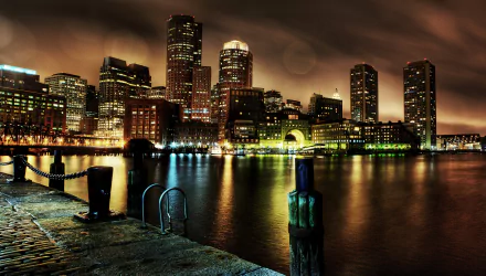 Night view of Boston's illuminated skyscrapers and city lights reflecting on the water, showcasing a vibrant man-made urban landscape in the USA.