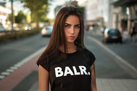 Brunette model Marlen Valderrama Alvaréz with tattoos stands confidently on a city street, captured in sharp focus with a blurred background in this HD desktop wallpaper.