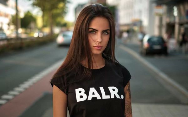 Brunette model Marlen Valderrama Alvaréz with tattoos stands confidently on a city street, captured in sharp focus with a blurred background in this HD desktop wallpaper.