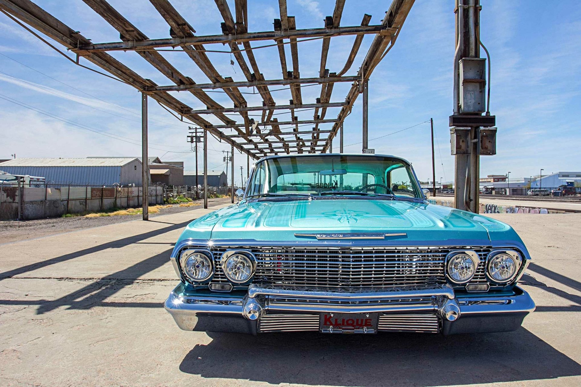 Front view of a turquoise Chevrolet Impala lowrider classic car parked under a metal structure, featured as an HD PC desktop wallpaper and background.
