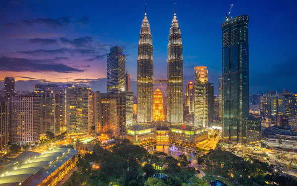 Night view of the illuminated Petronas Towers and surrounding skyscrapers in Kuala Lumpur, Malaysia, showcasing the city's vibrant urban skyline.