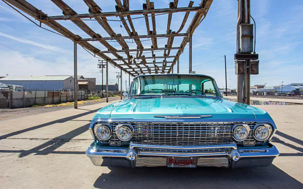 Front view of a turquoise Chevrolet Impala lowrider classic car parked under a metal structure, featured as an HD PC desktop wallpaper and background.