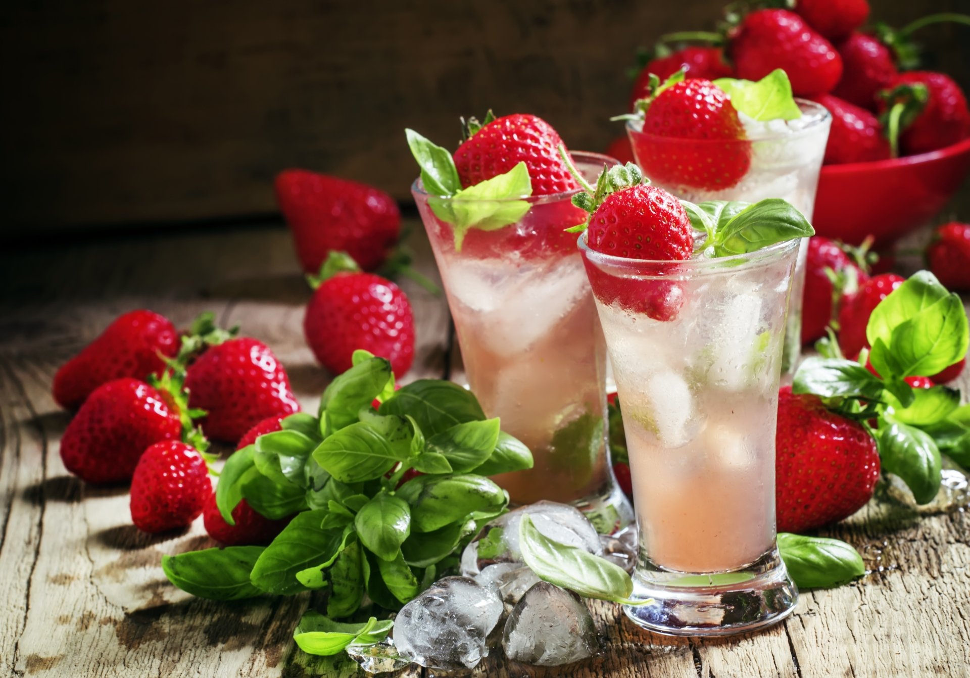 A vibrant 4K Ultra HD still life of fresh strawberries, ice cubes, and glasses of a refreshing strawberry drink on a rustic wooden surface.