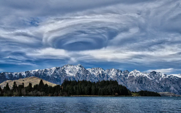 Dramatic vortex cloud formation swirls above snow-capped mountains and Lake Wakatipu in New Zealand, captured in stunning 8K Ultra HD.