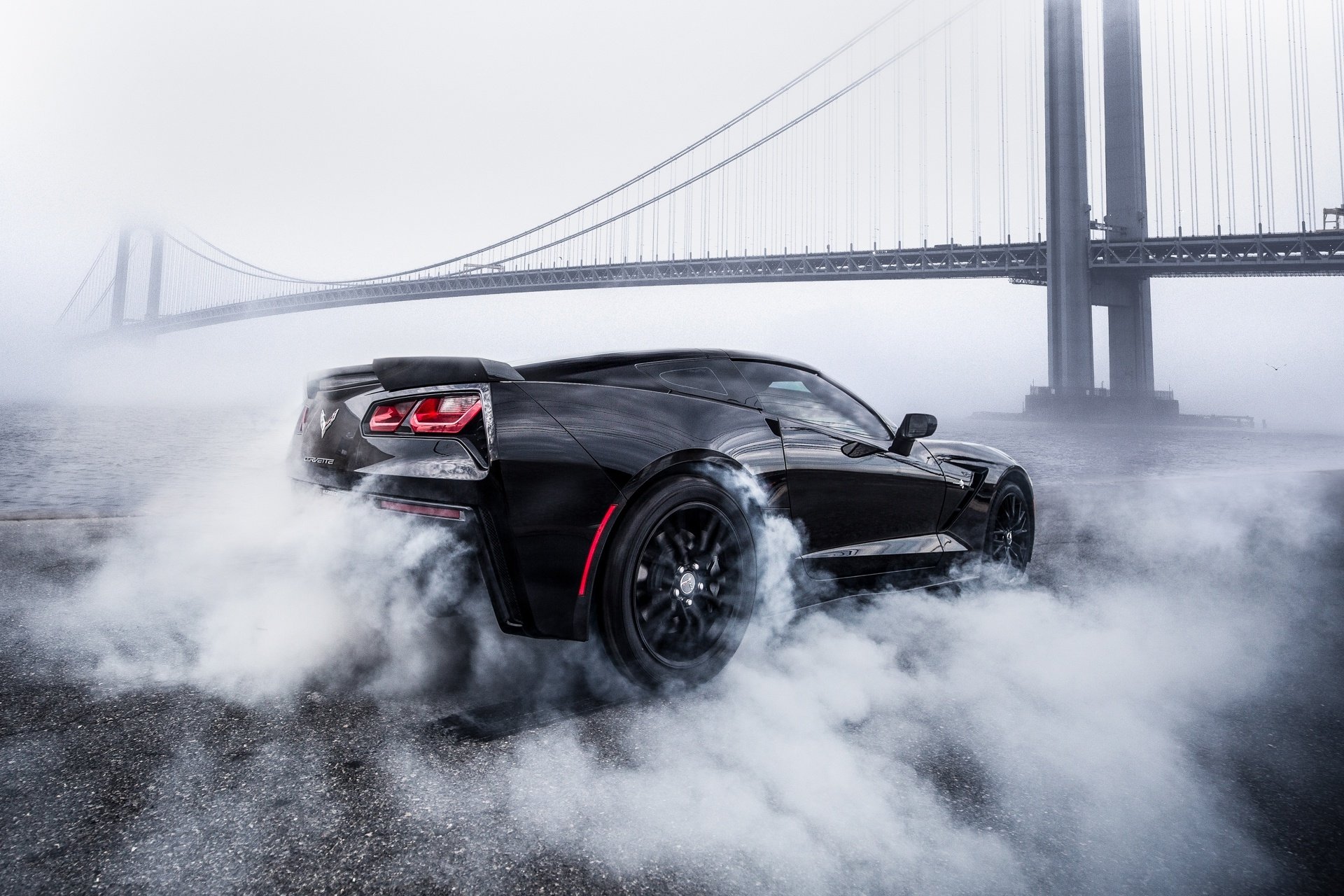 Black C9 Corvette burning rubber near a bridge HD Wallpaper