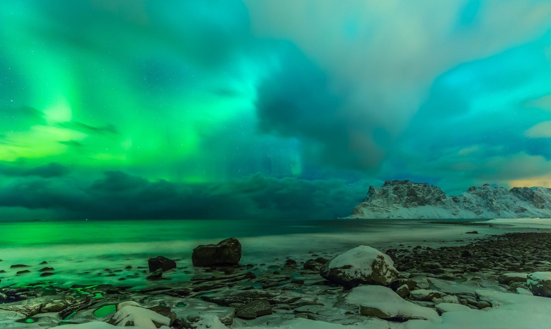 HD desktop wallpaper of a winter lake scene under a cloudy sky illuminated by the vibrant green aurora borealis, showcasing the serene beauty of nature.