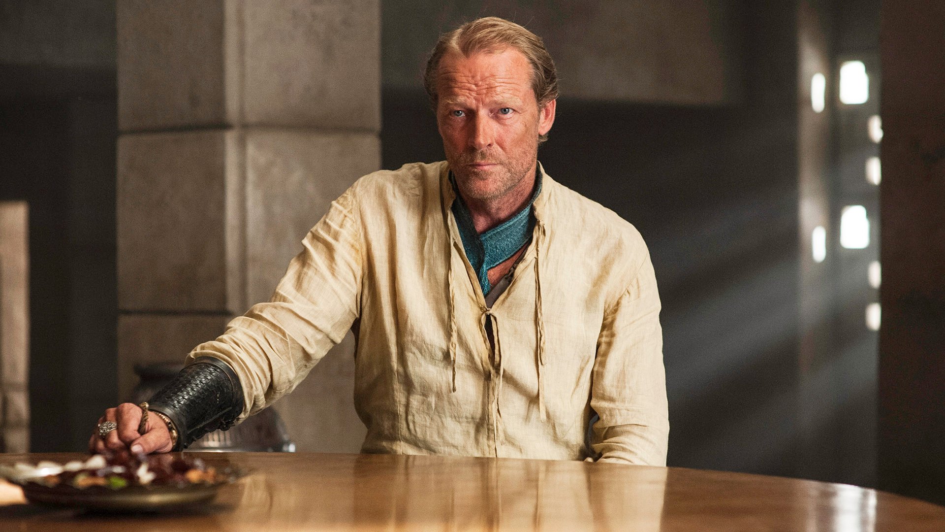HD desktop wallpaper: Jorah Mormont from the TV show Game of Thrones — a stern, bearded man in period costume seated at a wooden table.