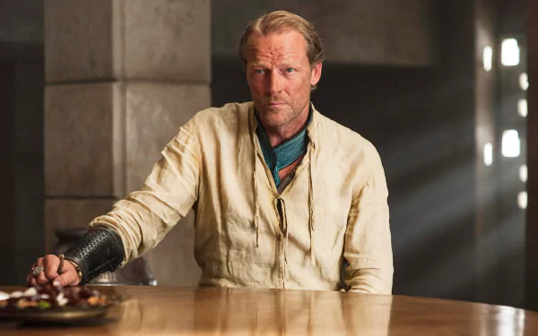 HD desktop wallpaper: Jorah Mormont from the TV show Game of Thrones — a stern, bearded man in period costume seated at a wooden table.