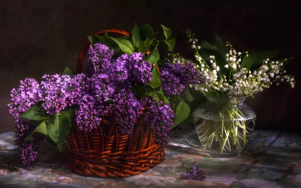 A still life HD wallpaper featuring white lily of the valley and purple lilac flowers arranged in a glass vase and a wicker basket against a dark background.