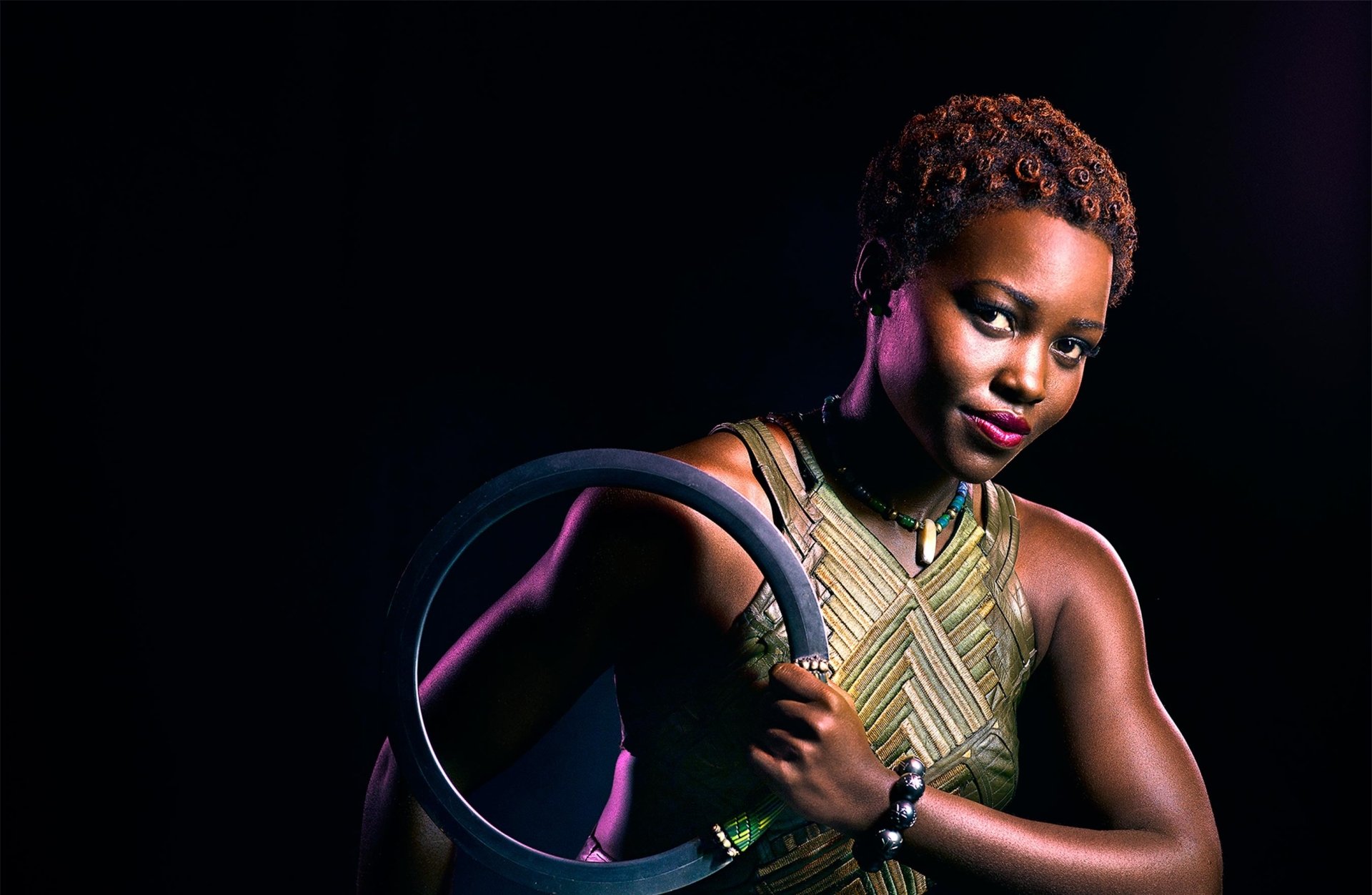 An HD desktop wallpaper featuring a character from the movie Black Panther, poised with a determined expression and holding a circular object against a dark background.